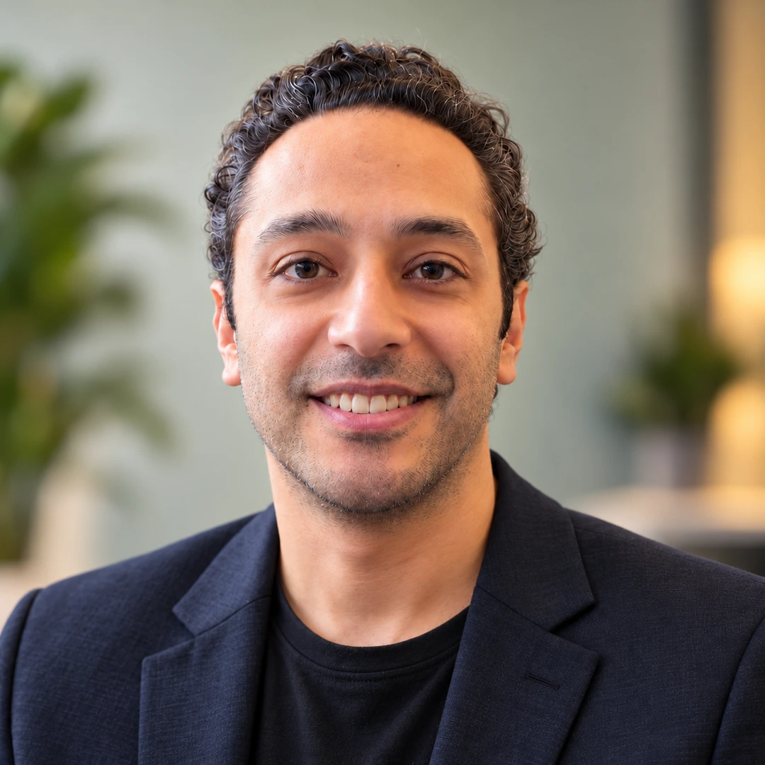 Professional portrait of Amir smiling in a dark blazer against a softly blurred background.